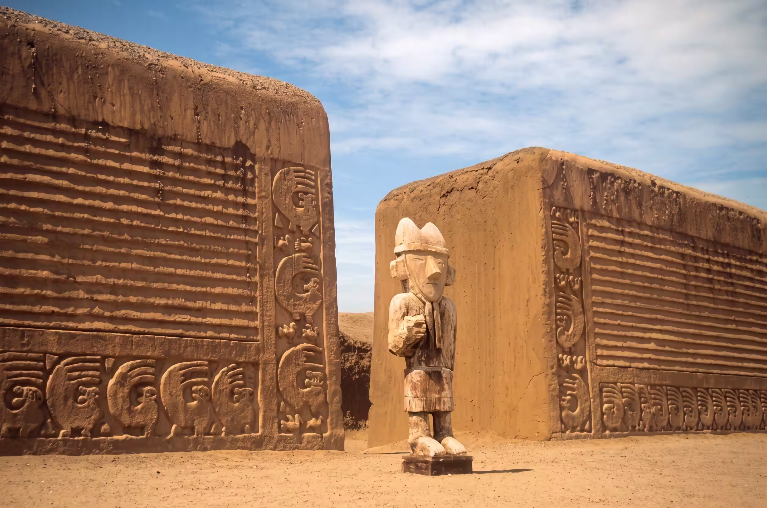 Muros de tierra con relieves y una figura de madera en Chan Chan, cerca de Trujillo.