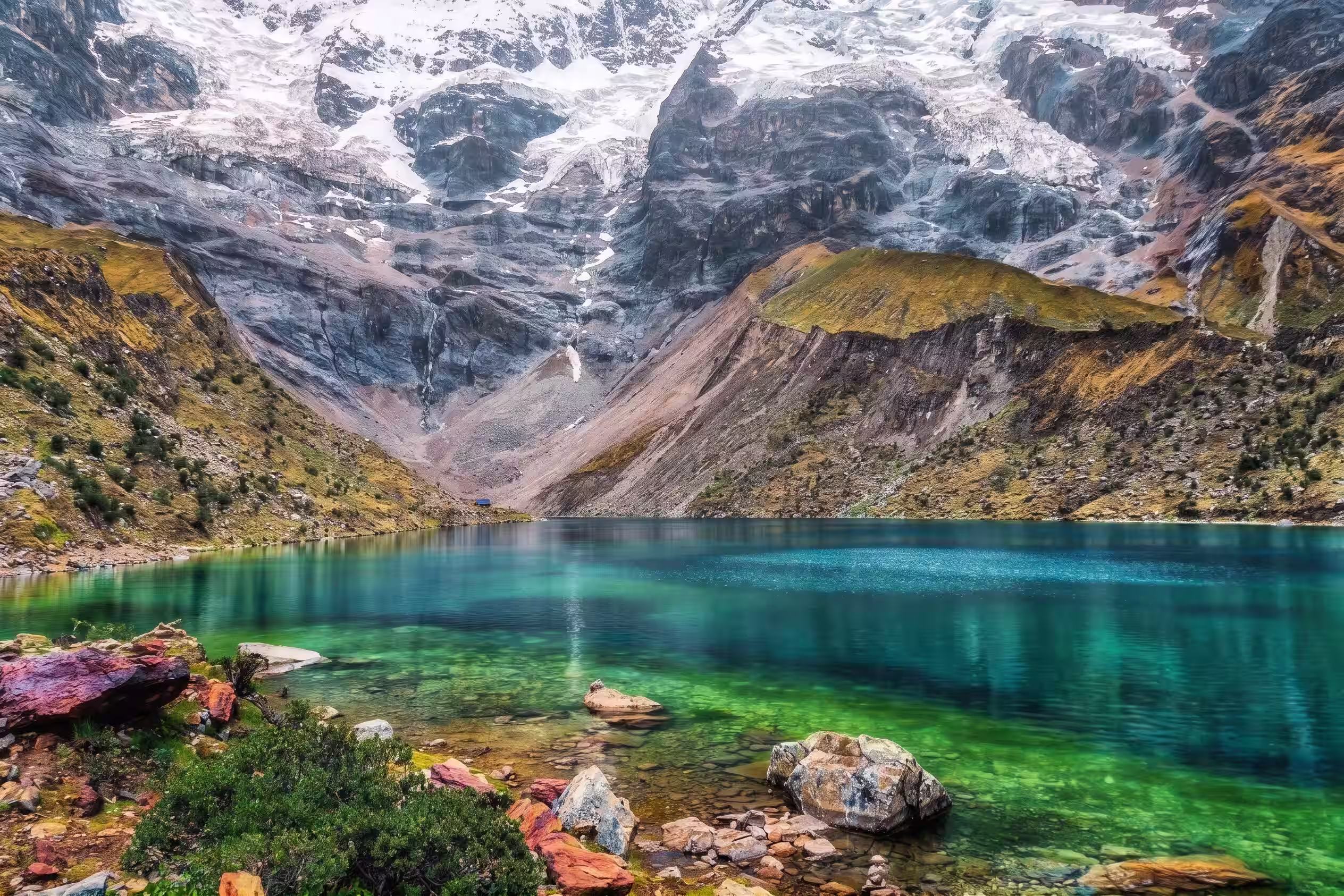 Aguas turquesas de la laguna Humantay al pie de laderas rocosas y montañas nevadas.
