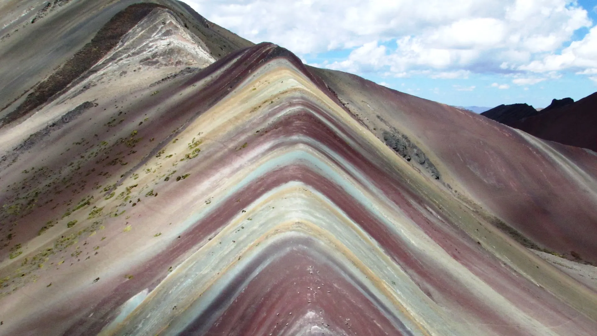 Franjas minerales de Vinicunca sobre las laderas montañosas, bajo un cielo con nubes.